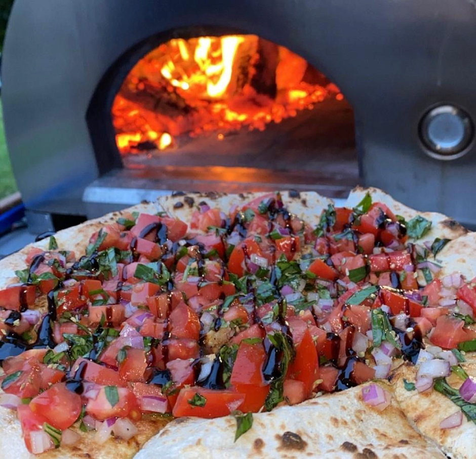Fresh bruschetta pizza in front of a roaring wood-fired oven